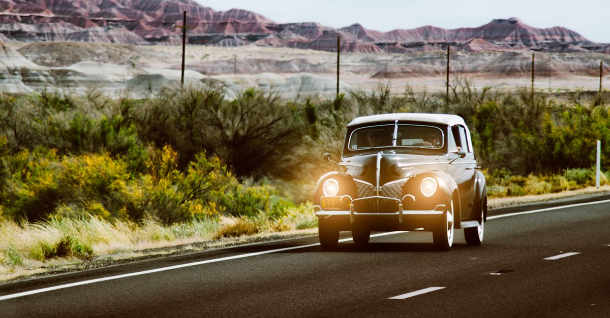 Vintage black car with headlights on driving through the scenic Arizona desert landscape.